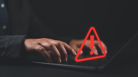 A person working on a laptop computer with a warning triangle to show that they need to take care