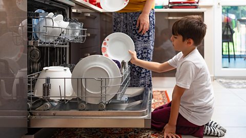 Boy helps mother to load the dish washer