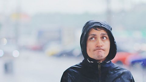 Man with his coat hood up looks dejected in the rain