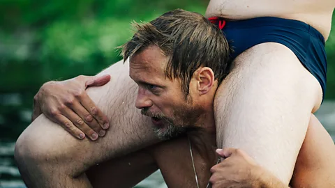 A24 Alexander Skarsgård carrying a man on his shoulders wearing only underwear in Pillion (Credit: A24)