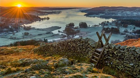 View down from hillside overlooking Lake Windermere with the sun rising on the horizon