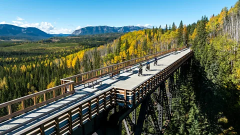 Peter O'Hara/ Travel Alberta A scenic view of people cycling or walking across a historic railway trestle above a deciduous forest (Credit: Peter O'Hara/ Travel Alberta)