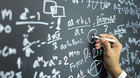 Hand writing complex mathematical equations and diagrams with white chalk on a large blackboard filled with algebraic formulas and geometric sketches.