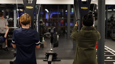Two teenage boys use resistance weight machines during a junior gym session