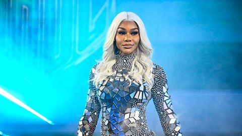 Jade Cargill stands against a blue backdrop, wearing clothing covered in tiny mirror fragments