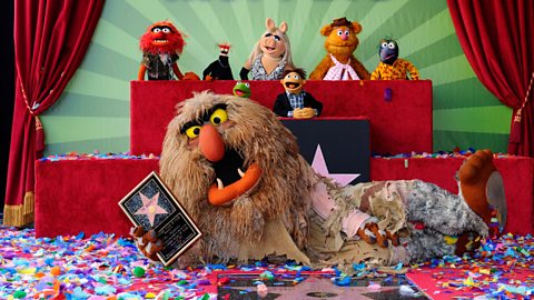 The Muppets at the unveiling of their star on the Hollywood Walk of Fame. Back row is Animal, Pepe, Miss Piggy, Fozzie Bear and Gonzo, all elevated. In front of them are Kermit and Walter, while Sweetums is laid on the floor by the star, holding a plaque, surrounded by confetti