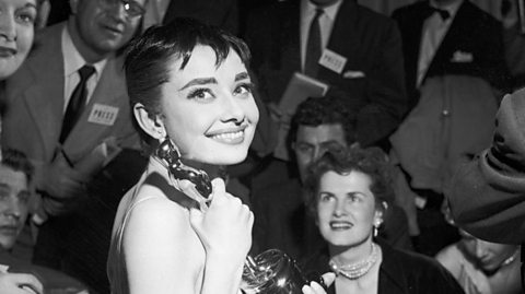 Audrey Hepburn holds her 1954 Oscar won for Roman Holiday, surrounded by members of the press