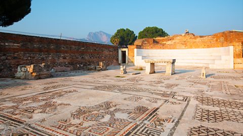The capital of the Lydian Kingdom. Ancient Sardis is located by the present day village of Sart in Manisa, Turkey. On a sunny day with a clear blue sky, walls surround a historic mosaic floor with pieces missing and an old marble bench at the centre