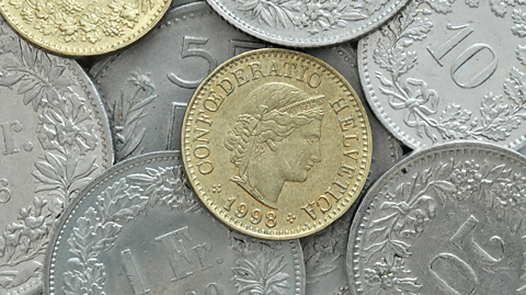 The 10 centimes coin, which has been produced by the Federal Mint Swissmint (Switzerland) since 1879. At the centre, the coin is gold and thin and sits on top of a pile of silver coins.