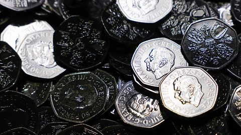 A pile of silver 50p coins with a portrait of King Charles, his side profile, printed onto the coins