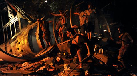 Lord of the Flies directed by Timothy Sheader at the Open Air Theatre Regent's Park in London. On set, young boys stand in the darkness around the ruins of a crashed plane