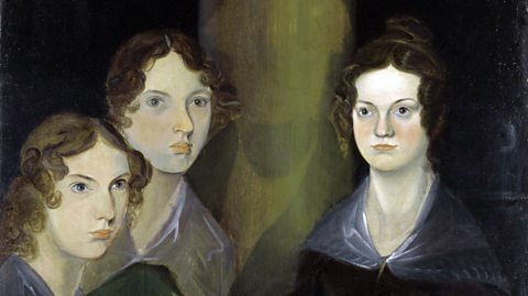 An oil painting of the Brontë sisters by Patrick Branwell Brontë. Anne, Emily and Charlotte all sit next to one another with blank expressions. They are all brunette with their hair in buns and curls falling loosely at the front. They wear dark dresses with blue coverings over their shoulders. The background is dark black and green