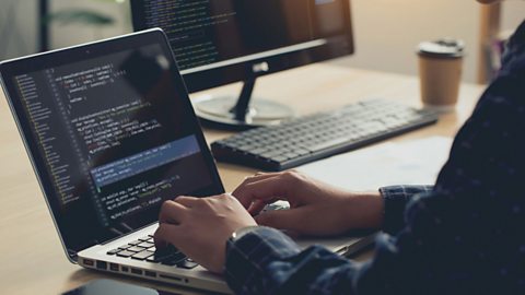 Hands are typing on a laptop keyboard with code displayed on the screen