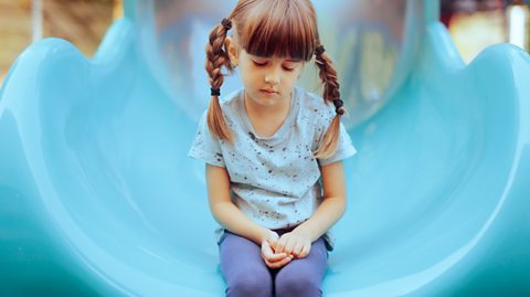 sad young girl sits on a playground slide