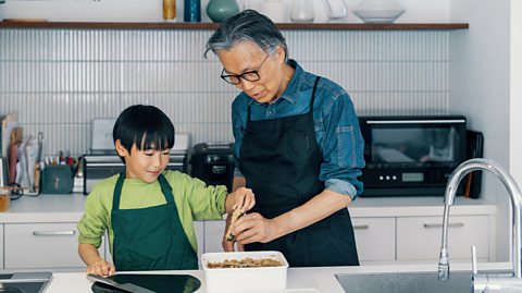 A grandfather and grandson prepare a meal together