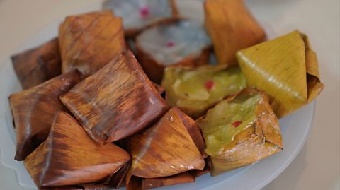 Studded dough pyramid dessert made with glutinous rice flour and sugar with banana in the centre. The light brown treats shaped like little pyramids are displayed in a white bowl