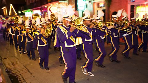 A march of people in purple playing brass instruments as part of Mardi Gras celebrations in the French Quarter, New Orleans