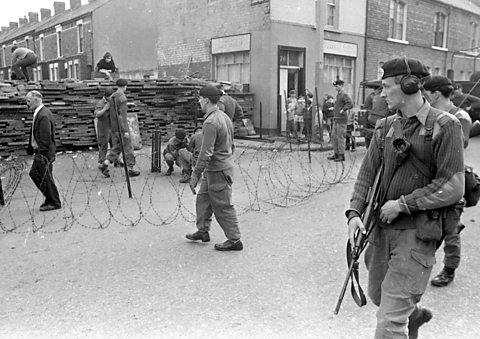 British Army troops patrol past a barricade, Northern Ireland, 1969.