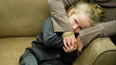 Sad little girl in school uniform in mother's arms on sofa 
