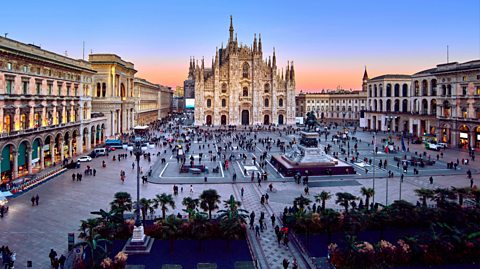 Aerial view of Milan Piazza Del Duomo at sunset in Italy. The cathedral stands at the centre of the busy square full of people, with old building lining the square