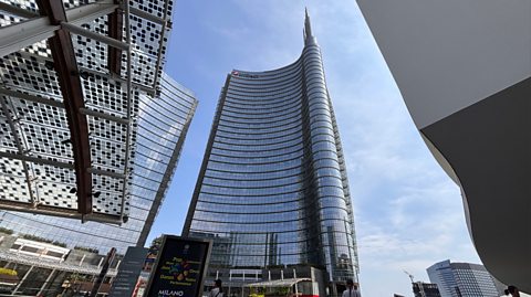 The Unicredit Tower, Milan, stands in the middle of a square full of tall buildings. The skyscraper has mirrored windows and a large spire pointing at the top