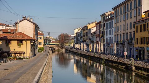 Part of the Navigli canal system in Milan. Either side of the canal on a clear blue sky day sits various old buildings, most painted in yellow and cream