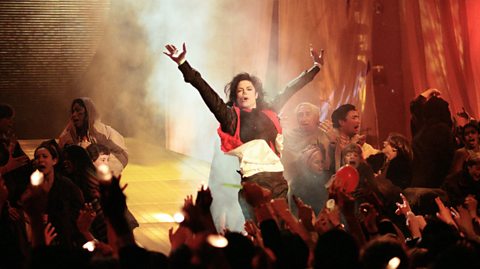Michael Jackson stood on stage, arms aloft, surrounded by a cast of children and adults while he performs Earth Song at the Brit Awards