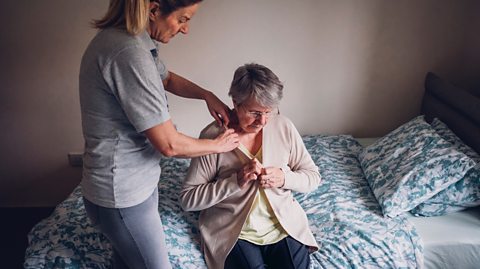 adult daughter assists mother in dressing at care home