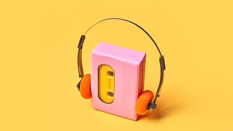 High angle view of a pink portable audio cassette player and vintage headphones on a yellow background