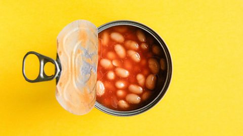 Open tin can full of baked beans on a yellow background