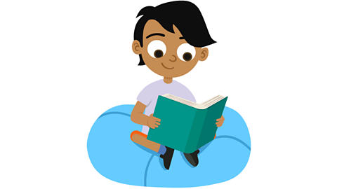 A young boy sitting on a blue cushion reading a book