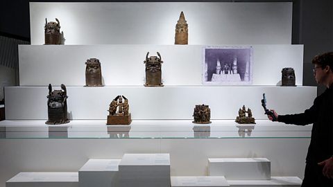 Different Benin bronzes on display in a museum. They include figurines and heads of Obas. 