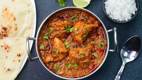 A dish of chicken tika masala with a side of rice and naan bread