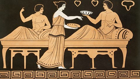 A picture drawn in the style of ancient Greek art. Two people are relaxing on long couches while another person brings them food on plates. The picture is decorated with simple shapes and patterns along the bottom and background.