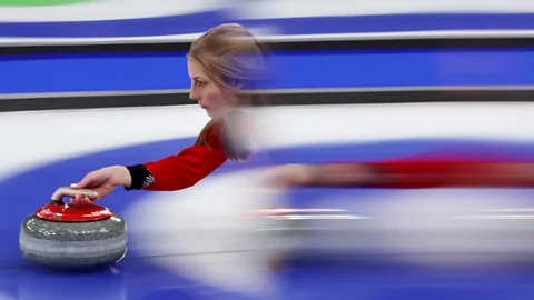 Carmen Mandato/ Getty Images A female curler about to release the stone. Her body is blurred but her face, hand and stone are in focus (Credit: Carmen Mandato/ Getty Images)