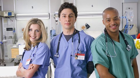 A press shot from the first series of Scrubs, showing, from left to right, Sarah Chalke as Dr Elliot Reid in blue scrubs, Zach Braff in blue scrubs as Dr John 'JD' Dorian and Donald Faison as Dr Christopher Turk in green scrubs