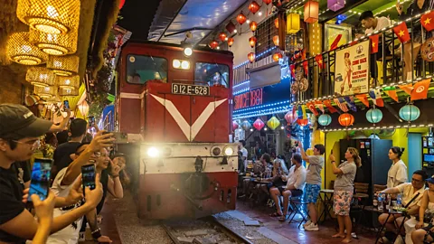 Alamy Tourists take photos as a train rushes through Hanoi's Train Street (Credit: Alamy)