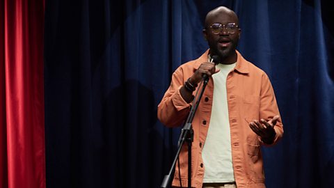 A photograph of a comedian on stage with a microphone in hand.