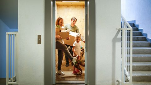 A mother, father and their daughter carrying items in a lift as the door begins to close