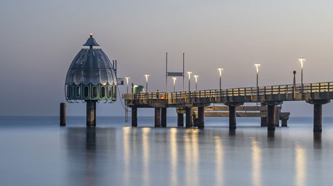 A view of a Tauchgondel lift at the end of a pier. Lights are on the pier, reflecting on the water