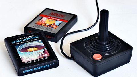 An Atari 2600 joystick with cartridges for Space Invaders and Ms Pac-Man alongside it, on a white backdrop