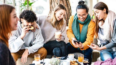 A multicultured group of friends looking at a phone and drinking coffee together
