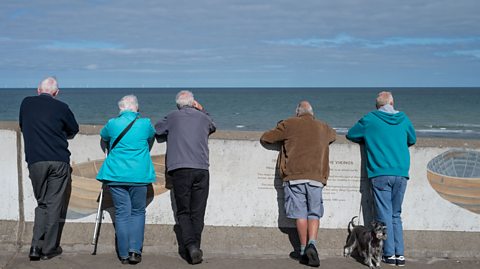 A group of senior citizens with a dog look out over the seawall towards the sea on September 17, 2024 in Sheringham, United Kingdom