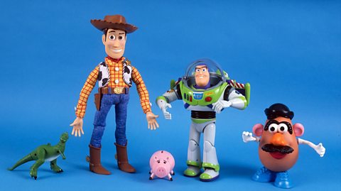 On a blue backdrop stand five Toy Story character toys. From left to right is Rex - a small green T-Rex dinosaur, Woody - a cowboy sheriff with brown boots, blue jeans, a yellow checked shirt with a cow pattern waistcoat and a brown cowboy hat, Buzz - an astronaut with a domed glass head helmet, a green and white space suit with buttons and wings and Mr Potato Head - a potato with blue shows, a black hat, eyes, pink ears, a nose, red lips and a black moustache