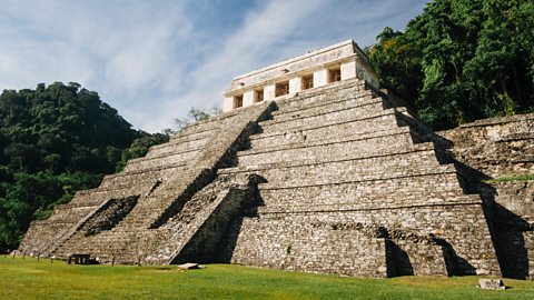 A big ancient stone pyramid-shaped structure with lots of steps stands in a green jungle. A small temple sits on top.