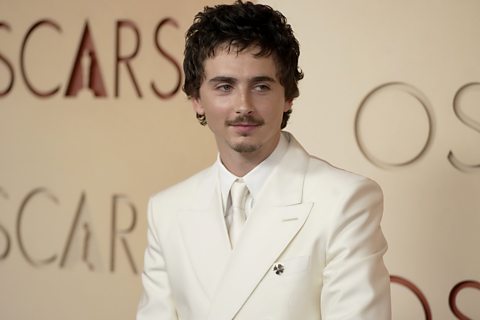 Timothee Chalamet at the Oscars wearing a white suit and tie with brown hair