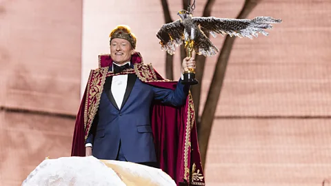 Conan O'Brien on stage at the Oscars wearing a crown, gown and holding an Oscar with a fake eagle of top of it (Credit: Getty Images)