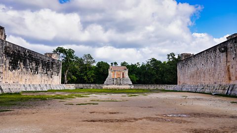 A big ancient stone court with very tall walls on both sides. There is a small temple-like building at the far end,