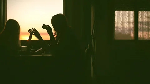 Getty Images Silhouettes of two people sitting at a table by a window at sunset (Credit: Getty Images)