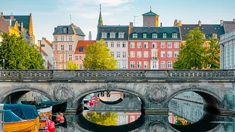 Getty Images Historic stone bridge over a canal with colourful townhouses and trees along the waterfront in Copenhagen (Credit: Getty Images)